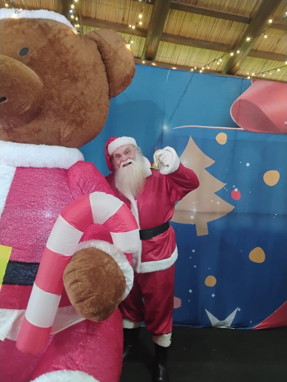 Papai Noel sorrindo com sino dourado em cenário natalino